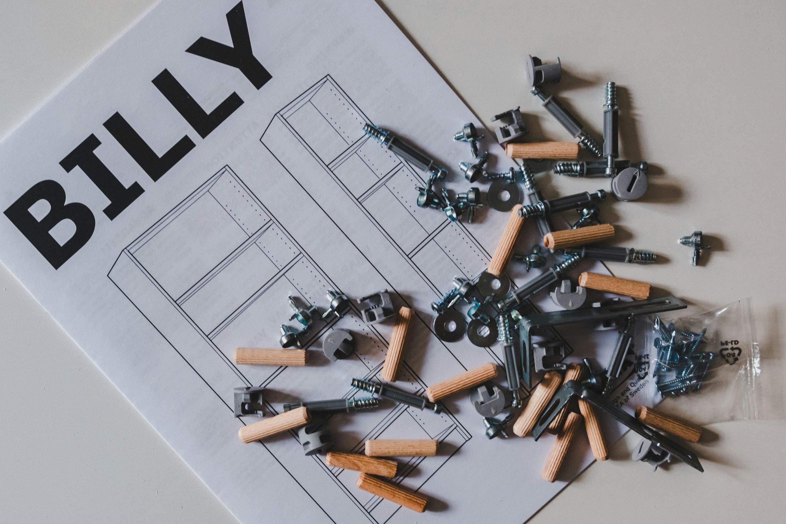 Scattered screws, dowels, and assembly parts lie on top of a BILLY bookshelf instruction manual, ready for furniture assembly