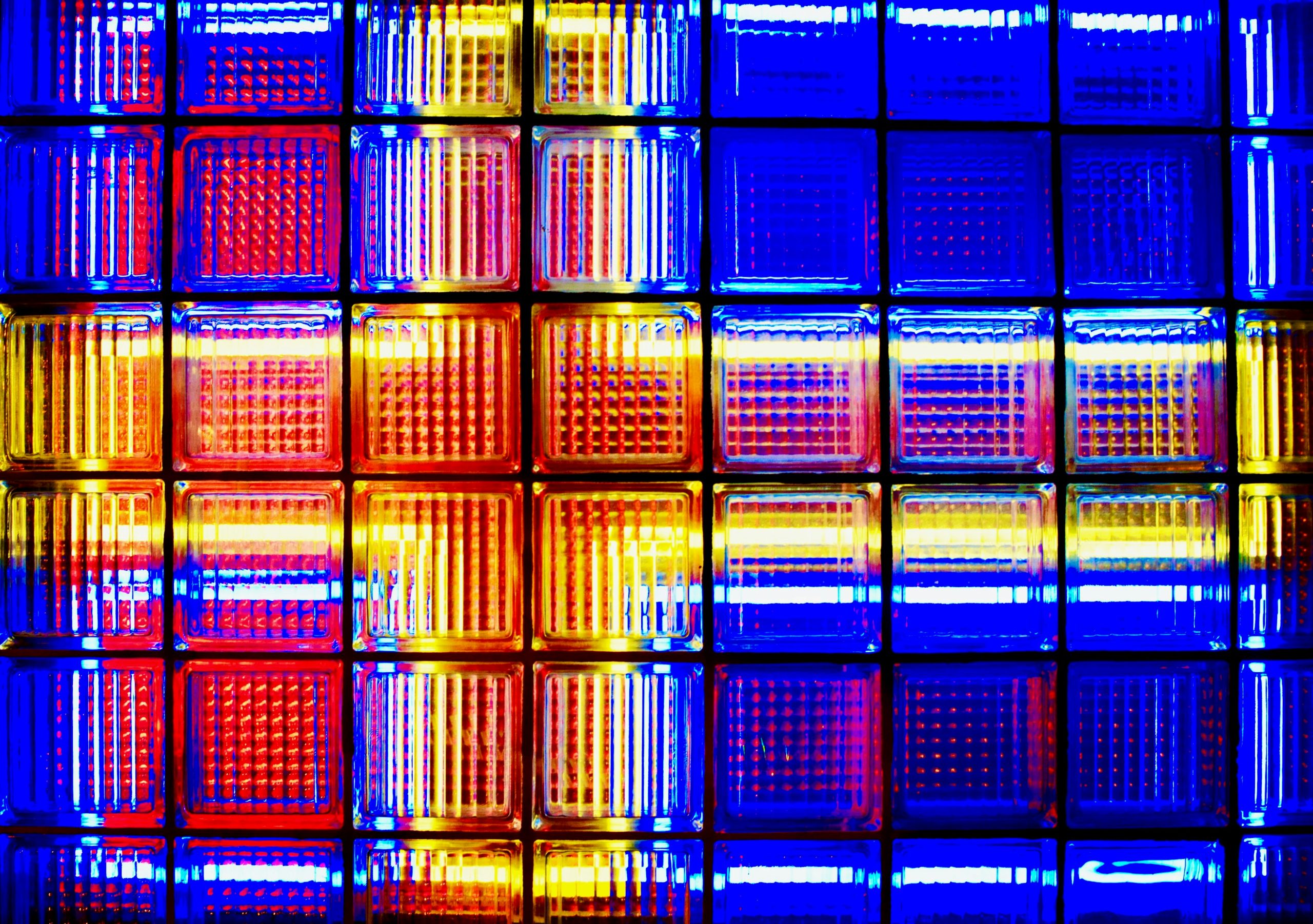 Abstract grid of colourful glass blocks in red, blue, and yellow hues, illuminated to highlight modular patterns